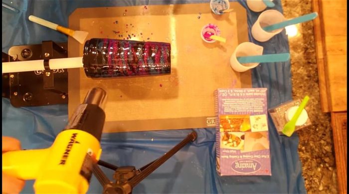 Using a heat gun to move neon purple and blue mica epoxy on a black galaxy tumbler