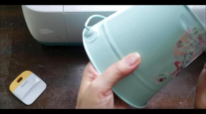 Slowly peeling transfer tape off a printed vinyl bunny on an aqua Easter bucket